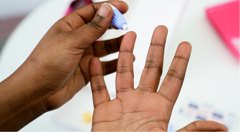 Close up image of hands holding a lancet using it to prick their finger. 