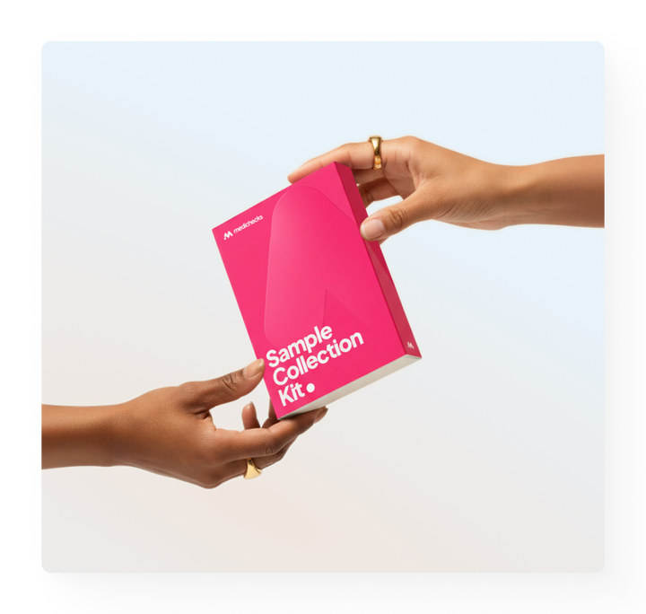Medichecks pink Sample Collection Kit box in-between two hands - one hand is passing the kit box, the other is accepting it